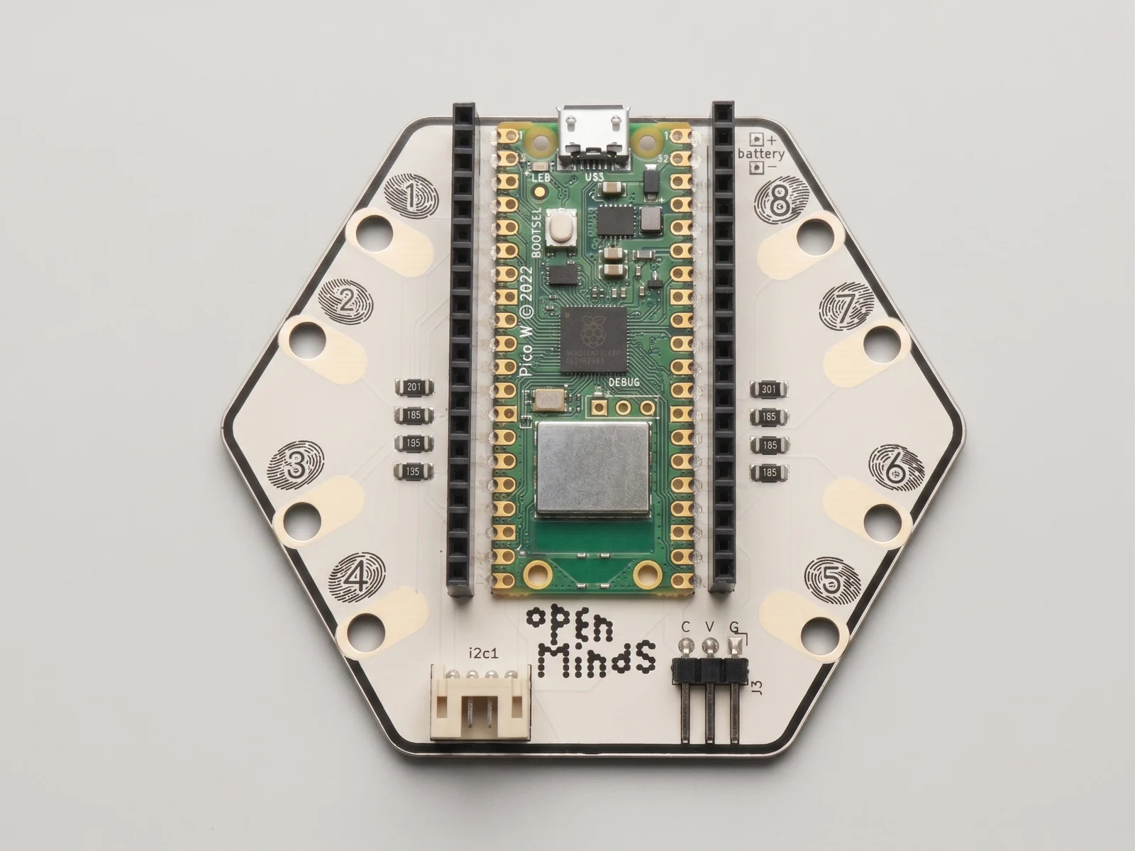 The hexagonal Open Minds main board from above, eight numbered capacitive-touch pads around the edge, the I2C connector along the lower edge, and the dot-matrix Open Minds logo.